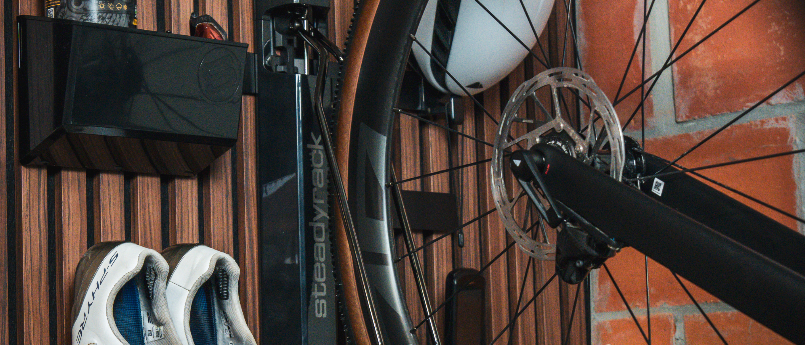 A close up of a bike in a rack with black storage components attached, on a wooden slat wall. 